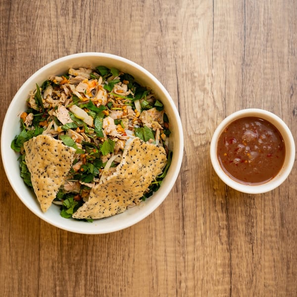 A bowl of Vietnamese chicken salad with herbs and crispy sesame crackers, next to a dipping sauce.