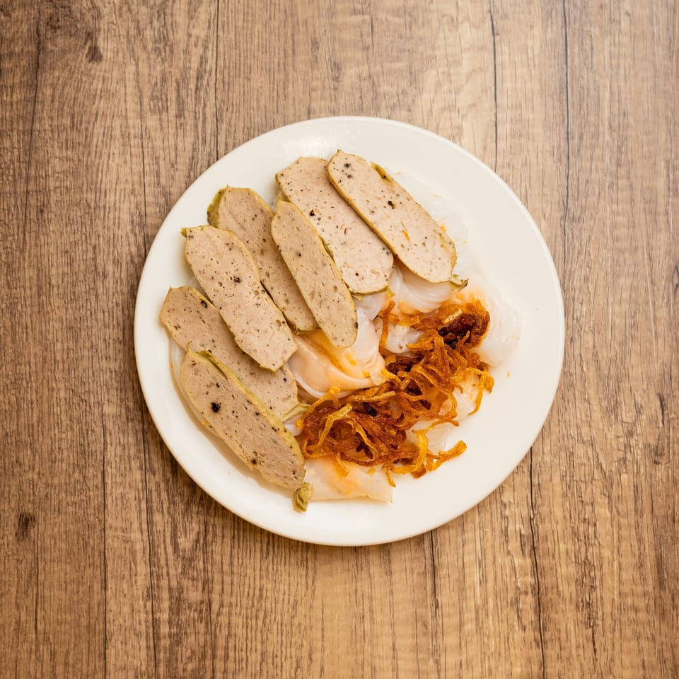 White plate with sliced Vietnamese pork sausage, rice noodle sheets, and crispy fried shallots.