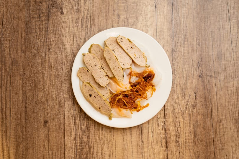 White plate with sliced Vietnamese pork sausage, rice noodle sheets, and crispy fried shallots.