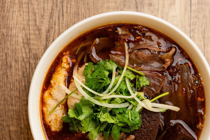 Close-up of a bowl of spicy Vietnamese bun bo Hue soup with meat, cilantro, and onions.