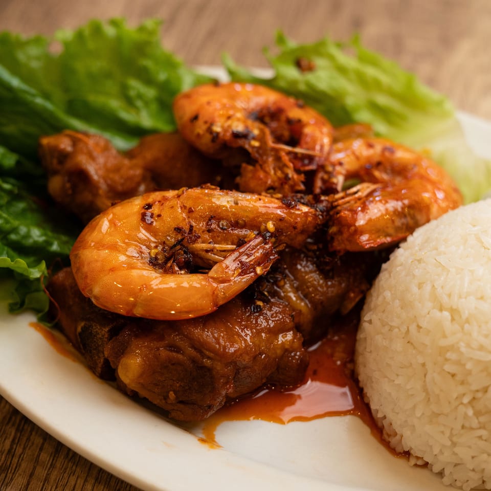 Spicy shrimp and ribs with white rice and lettuce on a white plate.