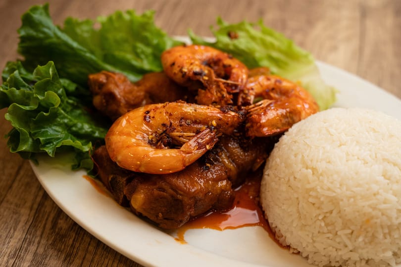 Spicy shrimp and ribs with white rice and lettuce on a white plate.