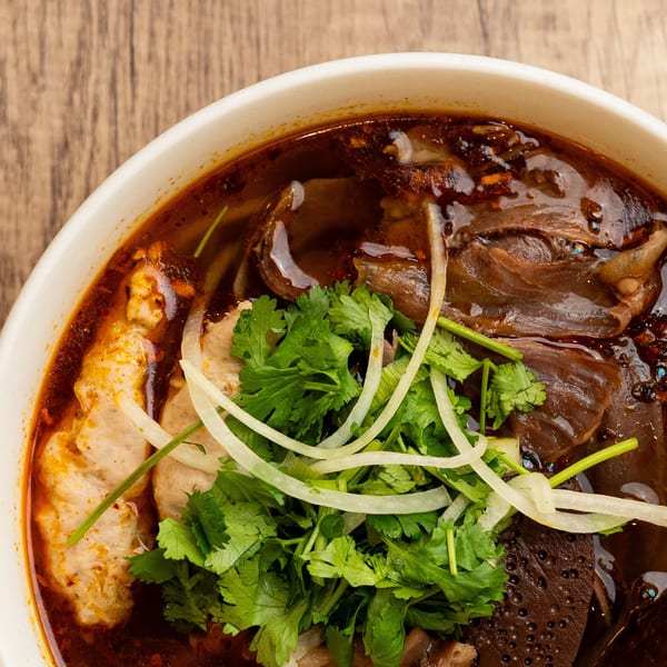 Close-up of a spicy Vietnamese noodle soup with various meats, herbs, and broth.